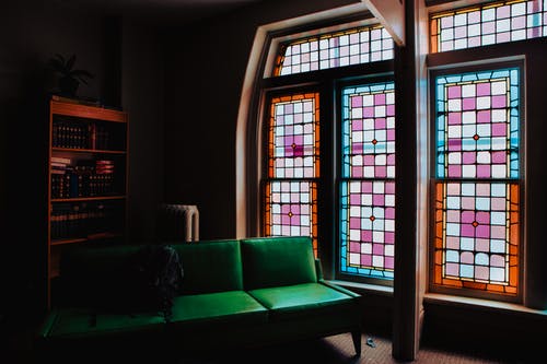 彩色玻璃窗旁边的绿色皮革沙发 · 免费素材图片