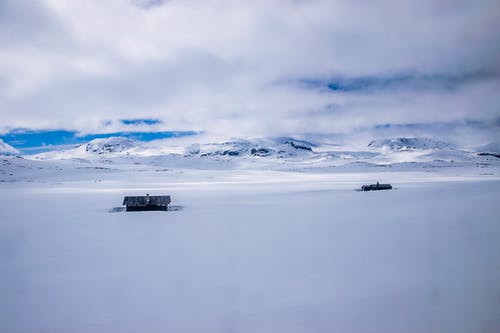 两栋房子在白雪皑皑的山脉附近的多云的天空下 · 免费素材图片