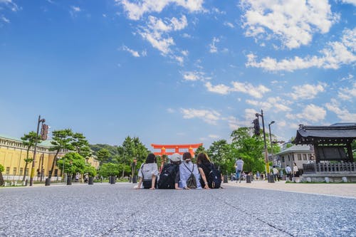 四个女孩坐在蓝蓝的天空下的灰色混凝土地板上 · 免费素材图片