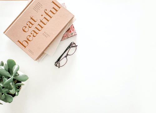 棕色镜框眼镜旁边吃美丽的书 · 免费素材图片