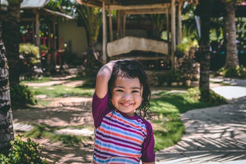 小女孩微笑着穿着紫色和多彩多姿的条纹的上衣 · 免费素材图片