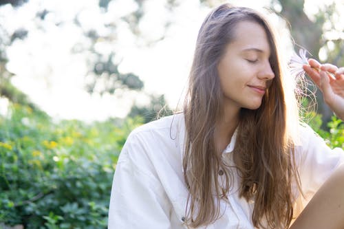 女人拿着白色的花瓣花时闭上眼睛 · 免费素材图片