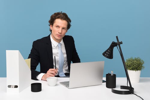 男人坐在桌子和灯与便携式计算机 · 免费素材图片