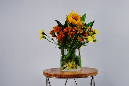 圆形棕色木制的桌子上的透明玻璃花瓶中的橙色，红色和黄色的花瓣花 · 免费素材图片
