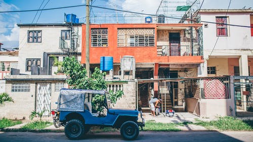 蓝色车辆停在橘子屋前的道路上 · 免费素材图片