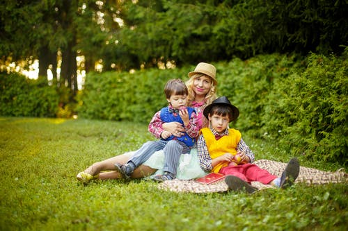 两个男孩在女人面前坐在绿色的草地上 · 免费素材图片