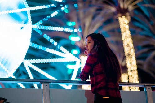 夜间靠在金属栏杆上的黑色和红色格子衬衫的女人的照片 · 免费素材图片