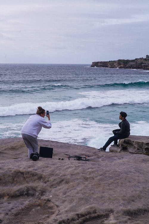 坐在海边旁边的灰色岩石上的男人 · 免费素材图片