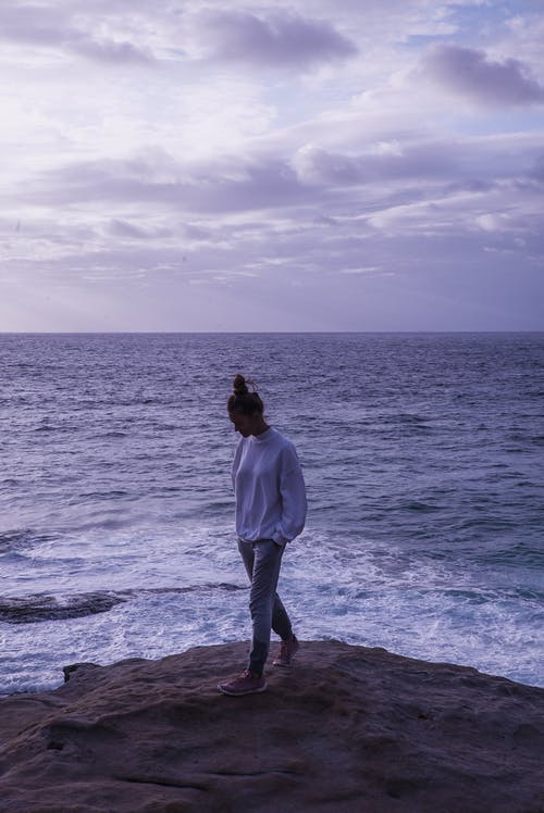 女人站在海洋附近的岩石上的照片 · 免费素材图片