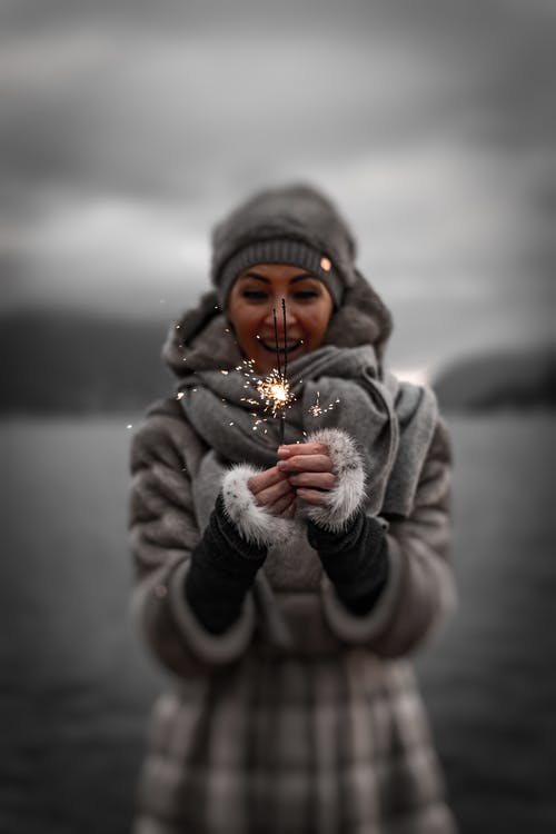微笑的女人在冬季服装拿着烟火的照片 · 免费素材图片