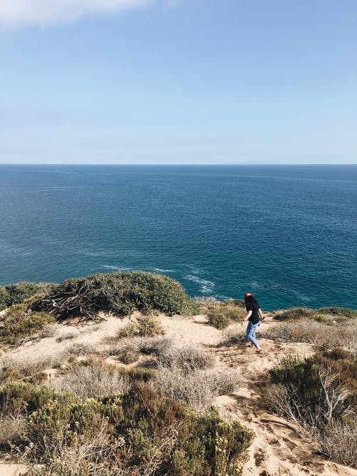 站在悬崖旁边海洋附近的女人 · 免费素材图片