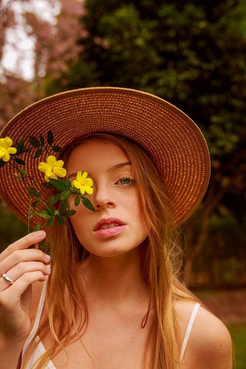 戴草帽，拿着黄色的花朵，靠近她的脸的女人 · 免费素材图片