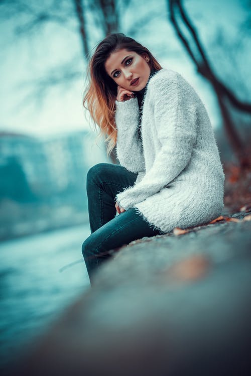坐在混凝土河岸上的白色毛衣的女人的照片 · 免费素材图片