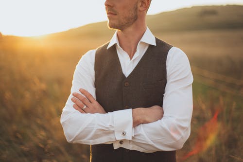 男人穿着白色礼服衬衫与黑色背心站在日落期间的草地上 · 免费素材图片