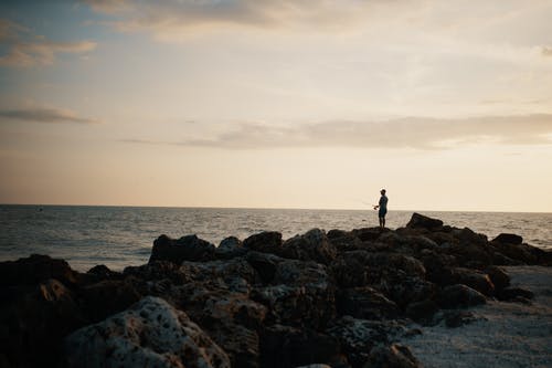站在多岩石的海岸上的人 · 免费素材图片