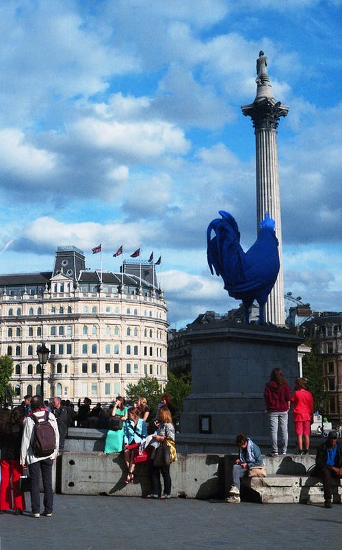 人们站在大厦的公鸡雕像下面 · 免费素材图片