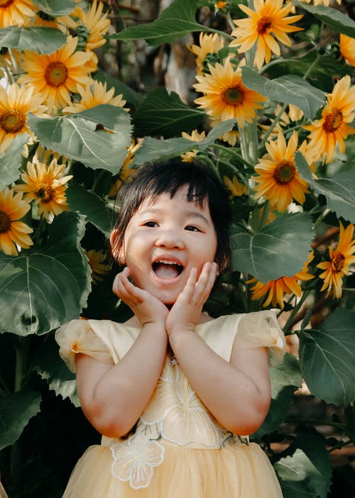 站在黄色的花朵附近的女孩的照片 · 免费素材图片
