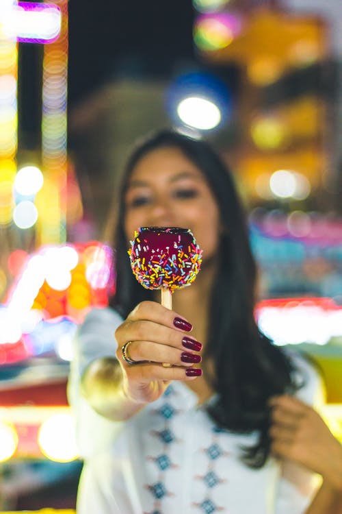 女人伸出糖果苹果的选择性焦点照片 · 免费素材图片