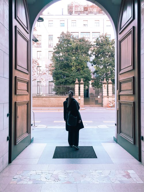 黑色大衣站在大布朗附近打开门的女人的照片 · 免费素材图片