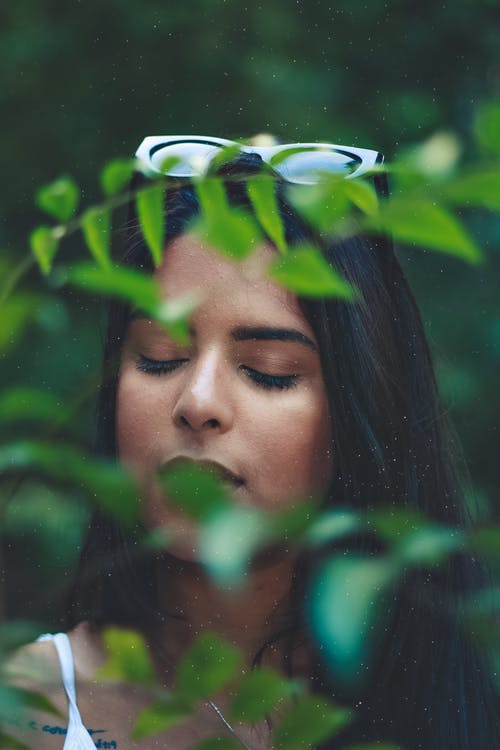 闭着眼睛站在绿叶植物后面的女人的照片 · 免费素材图片
