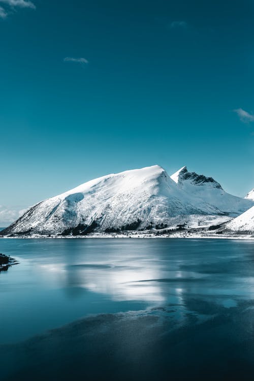 湛蓝的天空下平静的水体附近的白雪覆盖的山 · 免费素材图片