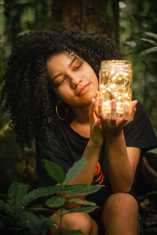 女人抱着透明的玻璃罐子灯附近绿叶植物 · 免费素材图片