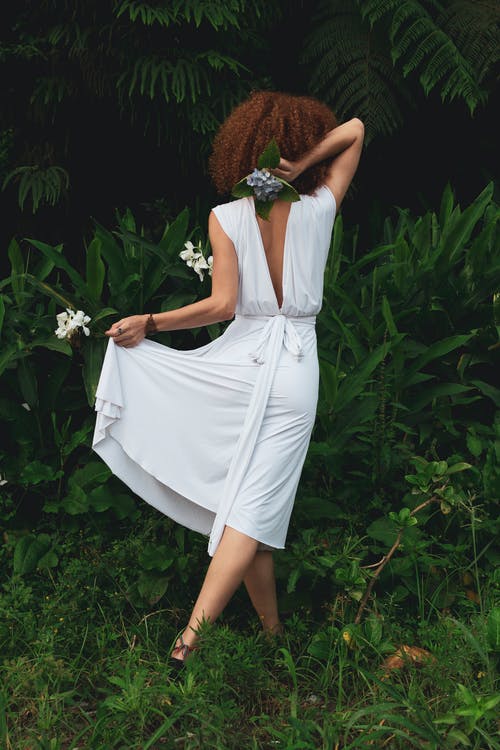 女人穿着白色的裙子站在植物旁边 · 免费素材图片