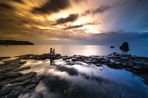 人坐在水体前的岩石上 · 免费素材图片