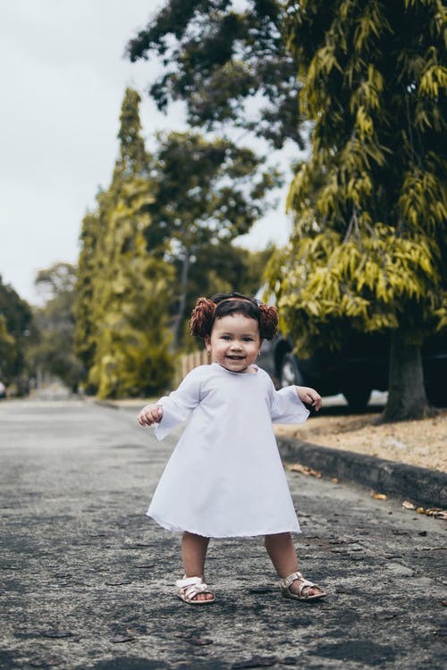 微笑宝贝女孩穿着白色的衣服站在路上 · 免费素材图片