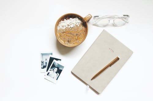 笔记本和笔旁边的棕色陶瓷杯 · 免费素材图片