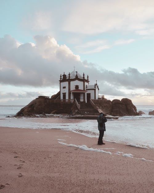 男子站在圆顶大楼附近的海滩 · 免费素材图片