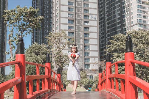 捧着鲜花站在桥上站在白色礼服和花冠的女人的照片 · 免费素材图片