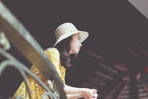 靠着金属栏杆望着太阳帽和花裙子的女人的照片 · 免费素材图片