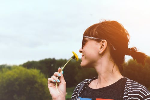 微笑的女人闻黄色花的侧视图照片 · 免费素材图片