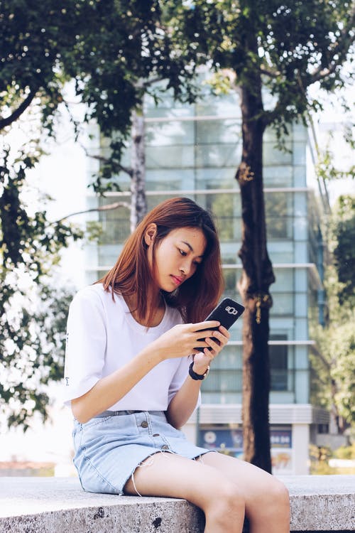 女人坐在混凝土长凳上使用她的手机 · 免费素材图片