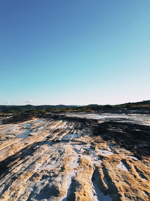 蓝蓝的天空下的棕色和黑色岩石地形 · 免费素材图片