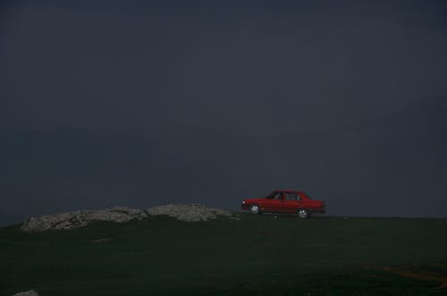 红色轿车的照片停在草地上，背景为雾山 · 免费素材图片