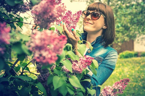 拿着淡紫色花的妇女佩带的太阳镜的照片 · 免费素材图片