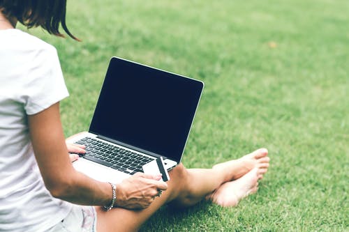 一个女人坐在草坪上持卡与mac的书本空气在膝上的照片 · 免费素材图片
