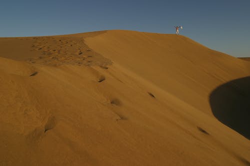 一个人站在沙漠的沙丘上的风景照片 · 免费素材图片