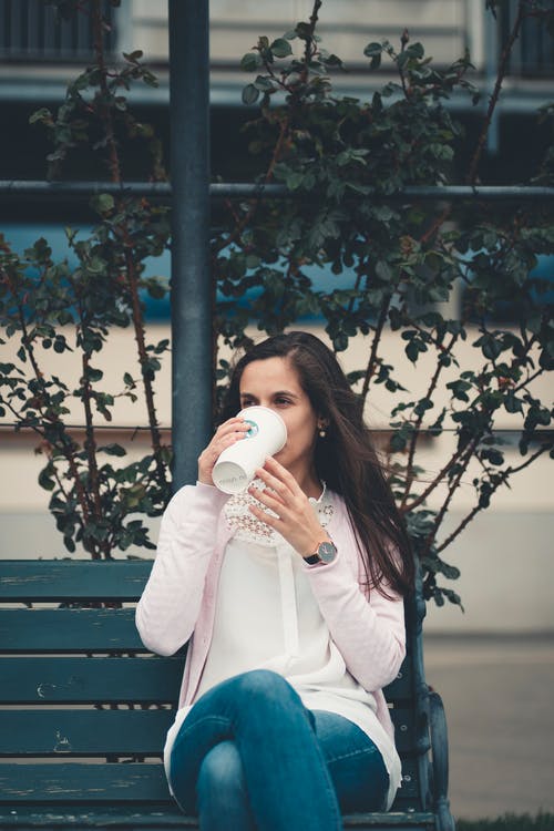 女人坐在长椅上，一边喝咖啡 · 免费素材图片