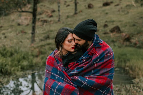 拥抱情侣在红色和黑色毯子覆盖户外的照片 · 免费素材图片