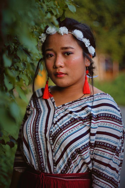 在绿色的树篱旁边摆姿势的白花冠冕的女人的选择性焦点肖像照片 · 免费素材图片