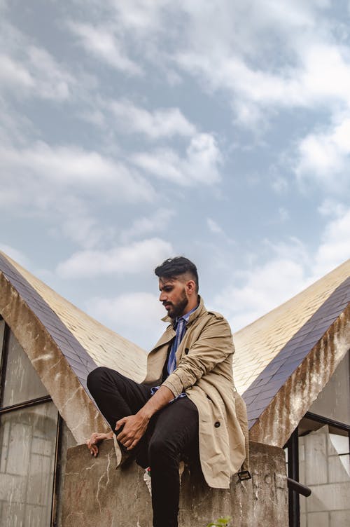 男子坐在灰色和棕色的屋顶表面 · 免费素材图片