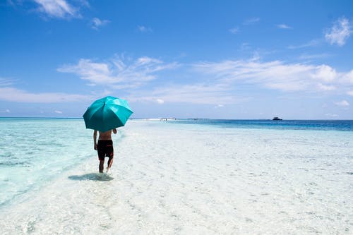 在海边拿着蓝伞走的人 · 免费素材图片