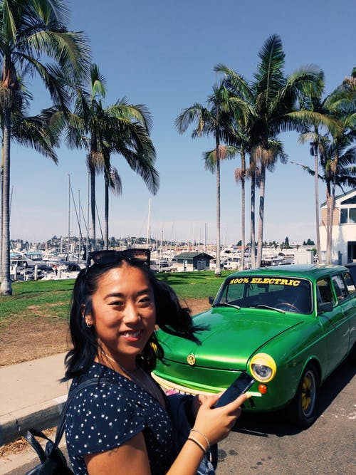 女人站在绿色的车附近微笑 · 免费素材图片