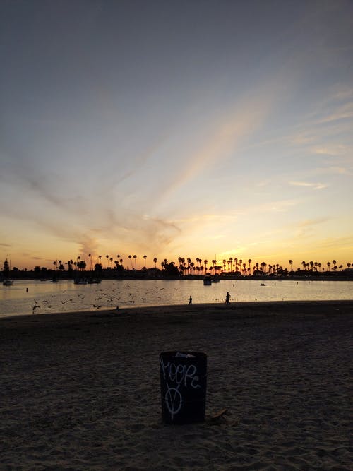 黑色和白色的垃圾桶，在海滨的蓝色和橙色的天空下 · 免费素材图片