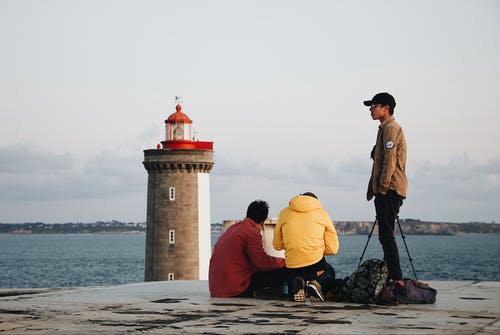 年轻人在靠近灯塔的海边的混凝土路面上 · 免费素材图片