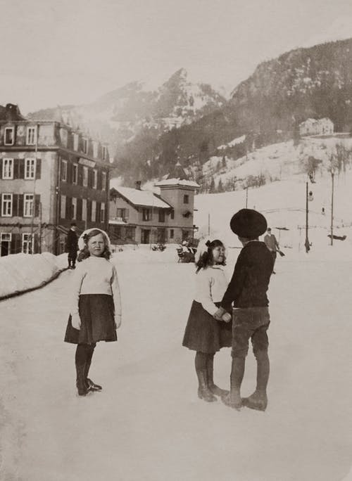 两个女孩和一个男孩站在白雪覆盖的路上的灰度照片 · 免费素材图片