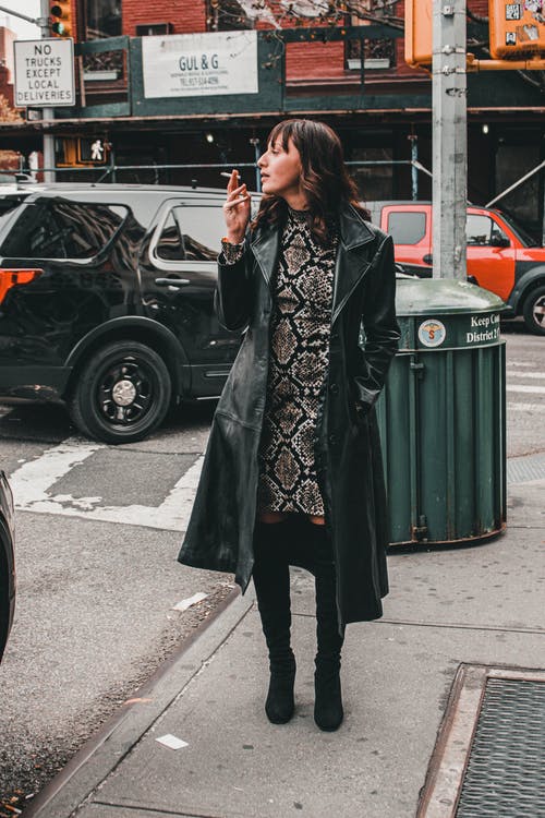 女人穿着黑大衣在大街上吸烟 · 免费素材图片